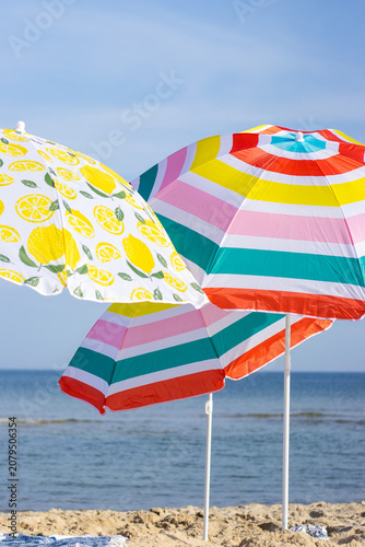 Colorful beach umbrellas with lemon and striped patterns stand on sandy shore, overlooking calm ocean waters under a clear blue sky