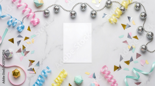 Blank card mockup on a marble flat lay with pastel ribbons, mini disco balls, and confetti for a festive party invitation template.