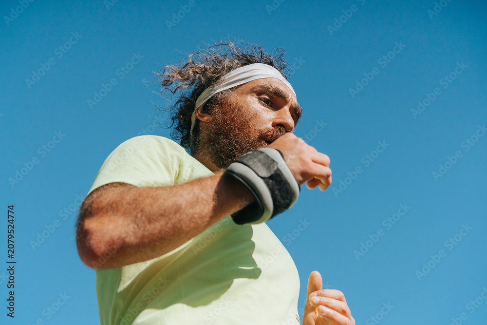 Obraz premium Athletic bearded man running with wrist weights outdoors