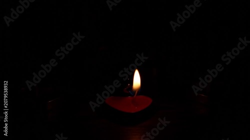 Multiple small red heart-shaped tealight candles sequentially ignite on dark wooden surface, growing from one flame to a full glowing group in complete darkness.