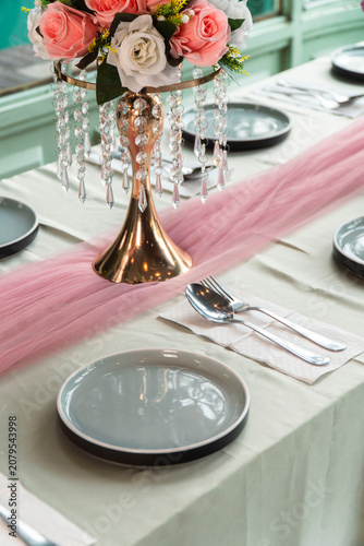 Elegant Table Setting: A beautifully arranged table set for a special occasion, featuring delicate flowers, crystal accents, and soft pink tulle runner, creating an atmosphere of refined celebration.