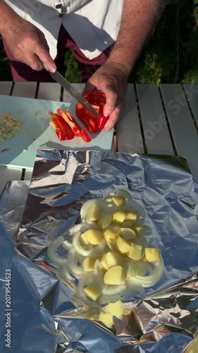 Close up of father hands slicing fresh red bell pepper on plastic cutting board at campsite table.