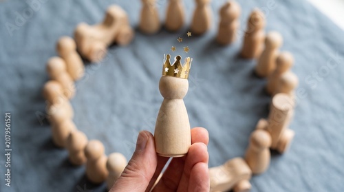 Hand Holding a Wooden Figure with a Golden Crown Symbolizing Leadership and Success in a Business Team Environment