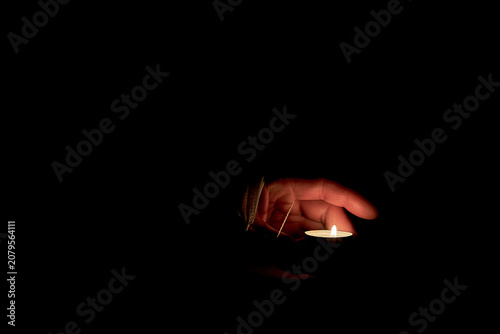 A human hand wrapped in a medical mask holds a burning candle.
