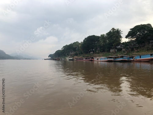 Εκτύπωση καμβά A serene riverscape featuring wooden boats anchored along the misty riverbank under a cloudy sky