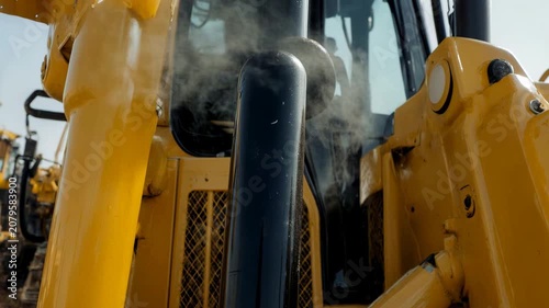 Close-up of heavy machinery exhaust pipe emitting smoke. Yellow construction equipment engine running outdoors. Industrial pollution concept