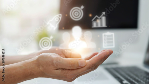Hands holding digital icons representing business growth, goals, and user profiles in a modern setting, symbolizing strategy and success