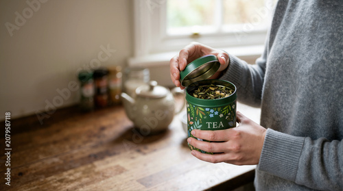 Person opening a green decorative tea tin. Loose leaf herbal tea in a metal canister on a kitchen counter