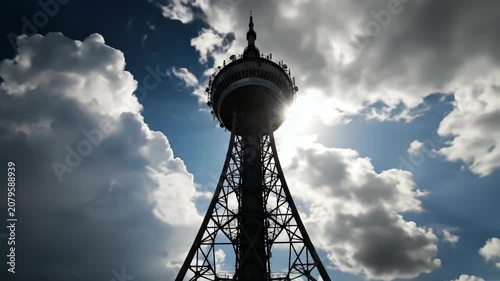 Dramatic silhouette of a communication tower with sun rays through the structure. Tall antenna under a cloudy sky. Global network and connectivity concept