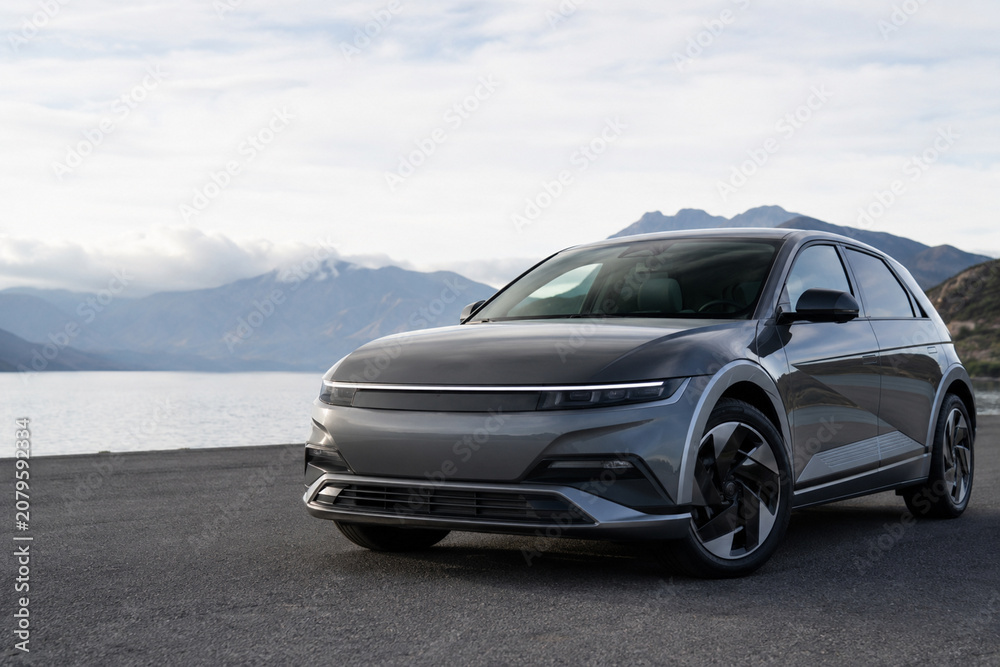 Naklejka premium Gray electric vehicle parked on asphalt road with mountain backdrop