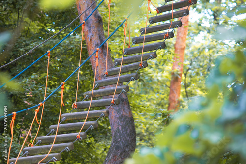 Rope park suspension bridge with dark wooden steps in summer forest