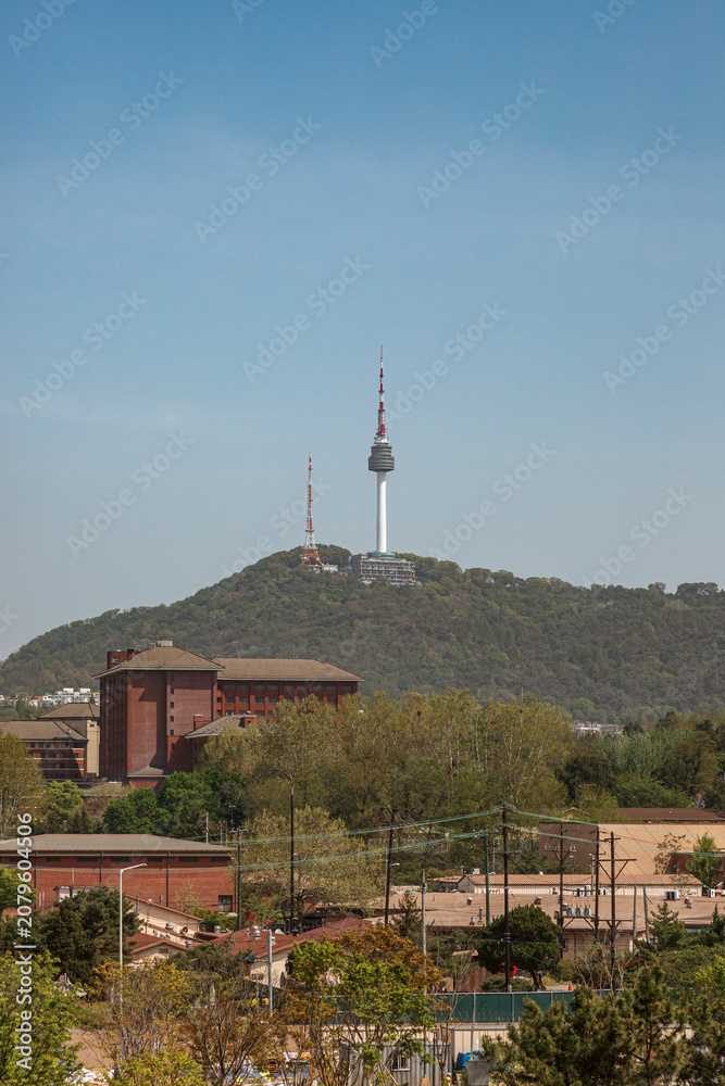 Obraz premium Vertical View of N Seoul Tower Standing on Namsan Mountain over City Buildings and Clear Blue Sky