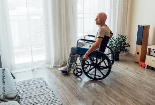 thoughtful disabled man in wheelchair looking out window at home representing loneliness depression physical disability rehabilitation recovery and accessibility challenges