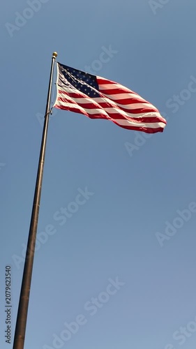 Low angle vertical shot of the United States flag waving in the wind against a clear blue sky