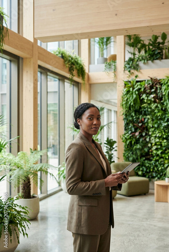 Professional businesswoman holding a digital tablet in a biophilic office. Corporate sustainability and ESG leadership concept