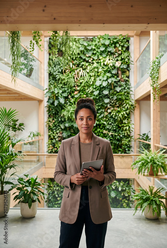 Professional businesswoman holding a digital tablet in a biophilic office. Corporate sustainability and ESG leadership concept