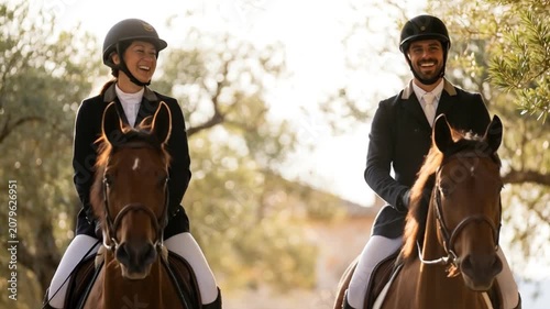 Laughing man and woman riding brown horses side by side through an olive grove at sunset