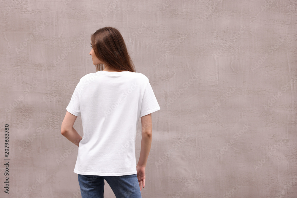 Obraz premium Woman wearing stylish white t-shirt near grey wall outdoors, back view. Space for text
