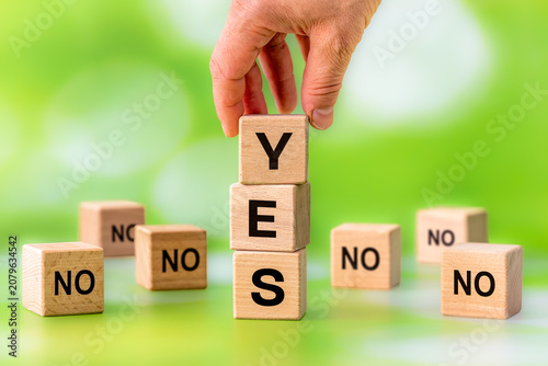 Foto Yes vs No with a hand stacking wooden blocks to spell Yes among surrounding No voices as a motivational business concept of fearlessness and conviction to one's own decisions despite bad advisors