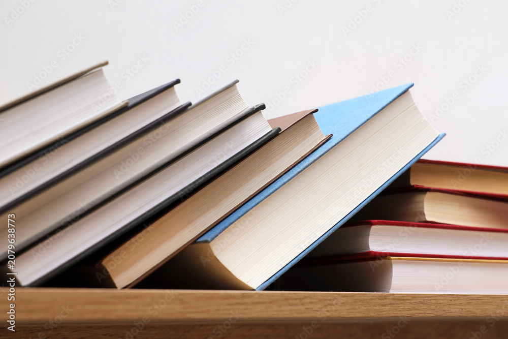 Fototapeta premium Different books on wooden shelf near white wall indoors, closeup
