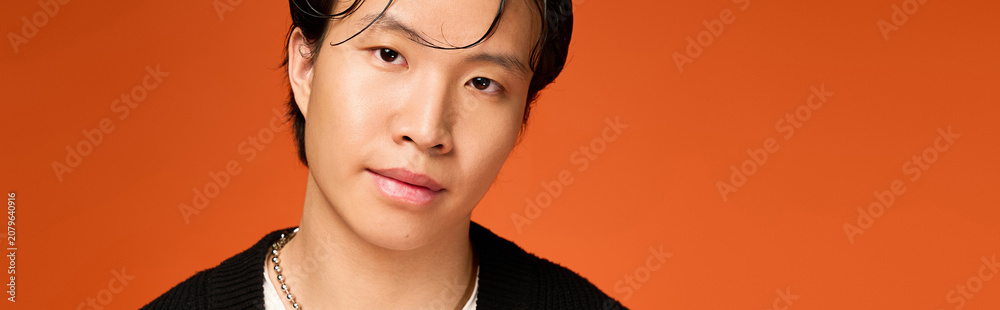 Fototapeta premium Stylish young man showcases modern fashion in vibrant orange studio setting