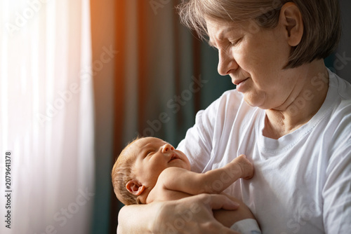 Obraz na plátně Grandmother gently holding a sleeping newborn baby in her arms, feeling the prof
