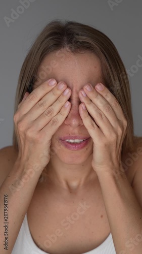 Young woman covering and gently pressing her eyes with hands, suffering from eye strain, fatigue or pain on a light grey background. Vision problem and stress concept
