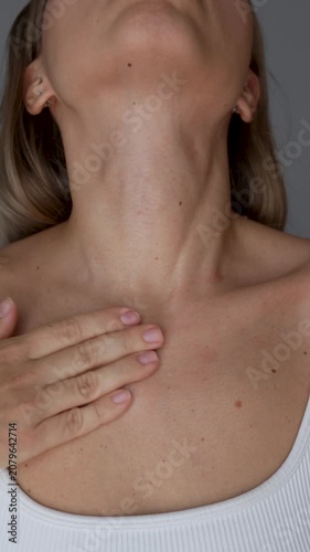 Young woman applying cream to neck and décolleté, moisturizing delicate skin as part of a daily beauty routine on a light grey background