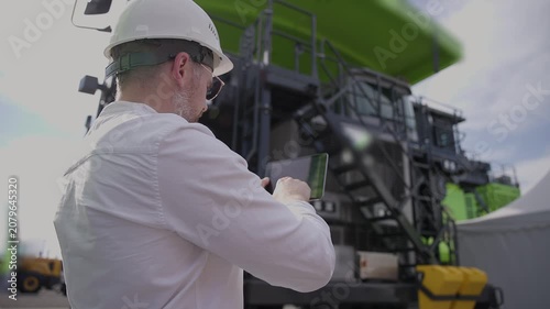 Engineer using tablet to inspect heavy industrial machinery and setting up and installing an AI-powered autopilot for mining trucks.