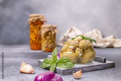 Pickled mushrooms in glass jar with basil and garlic