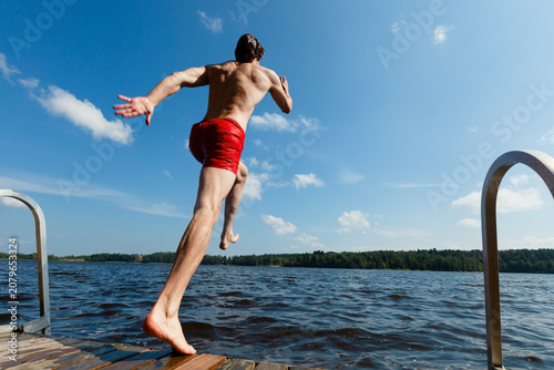 Фотография Man leaps off wooden dock into lake creating big splash on sunny summer day
