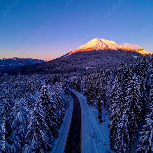 beautiful winter road with dark night road through forest and mountains, wintery scene at sunset