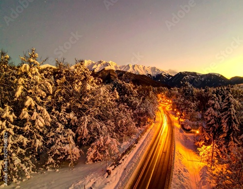 beautiful winter road with dark night road through forest and mountains, wintery scene at sunset