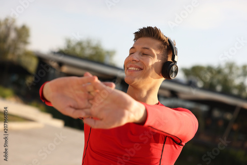 Happy man with headphones exercising outdoors on summer day