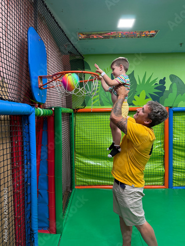 Father lifting son playing basketball in soft play area