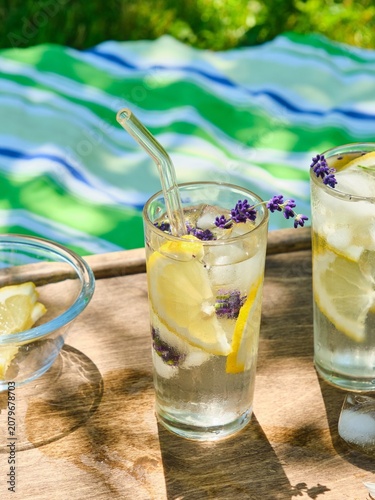 The process of preparing cold water with lemon and ice cubes in tall glasses outdoors in summer.