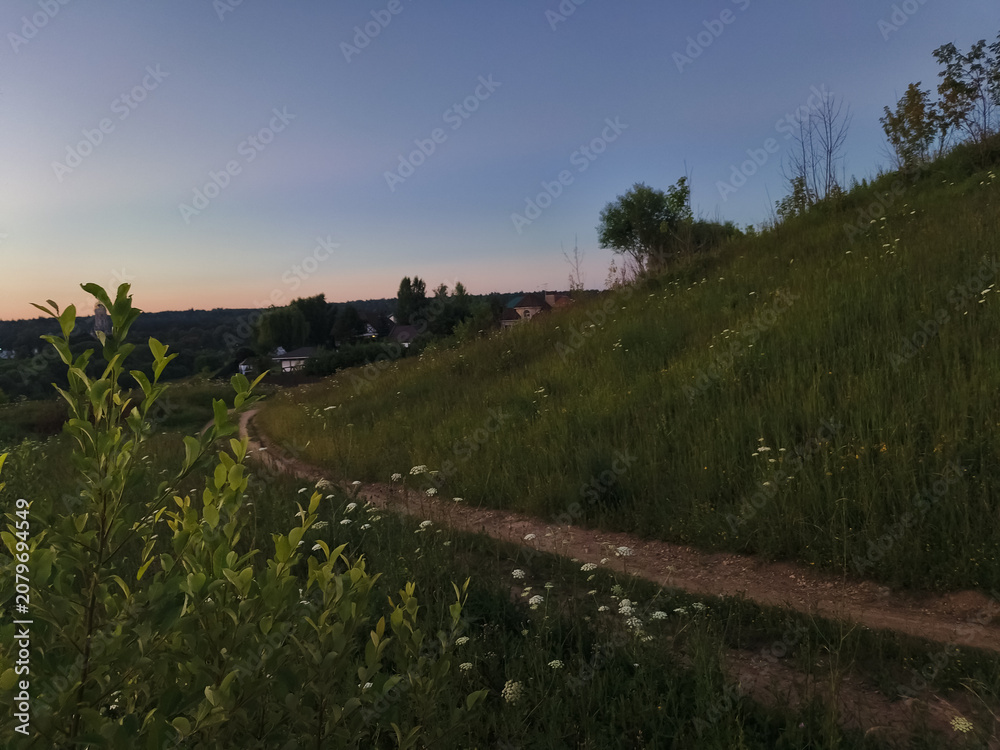 Obraz premium Green grass and blue sky in the wild in mountains road with meadow in evening sunset 