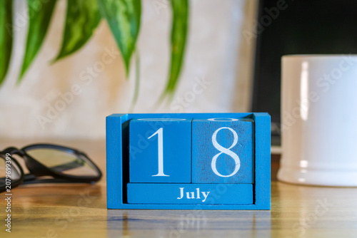 Konstfotografi Wooden perpetual calendar showing 18 July on office desk with coffee mug and wor