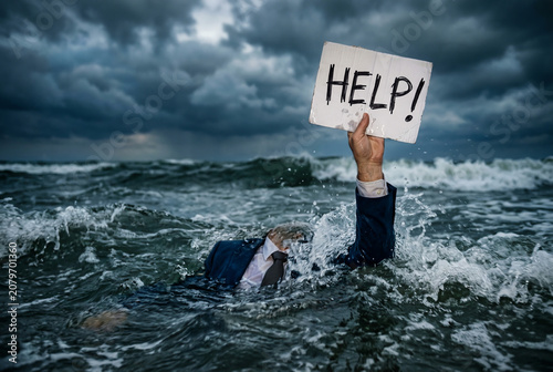 Businessman struggling in stormy ocean holding a Help sign, symbolizing crisis, financial distress, mental health challenges, desperation, rescue, survival, and hope.