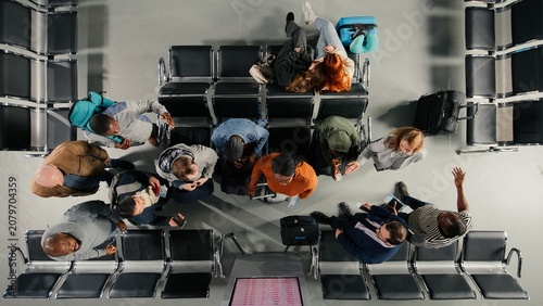 Foto Top down view of troubled tourists in airport distressed by plane delays shown on departure board, Passengers upset by canceled flights announcement on FIDS