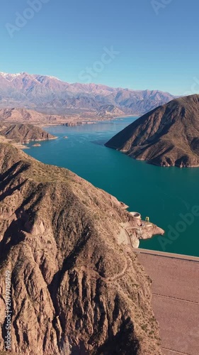 Drone vertical video over dam wall, turquoise Potrerillos lake and snowy mountains in Mendoza, Argentina