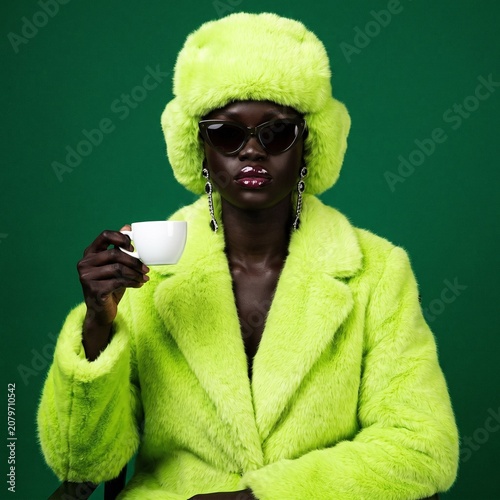 Young black woman wearing green fur coat and holding cup  