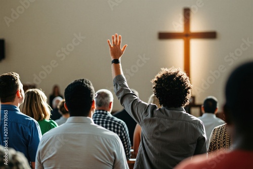 Man raises hand in church service with people. Wooden cross backlit, worshipful atmosphere. Faith, community, prayer, spirituality in religious gathering.