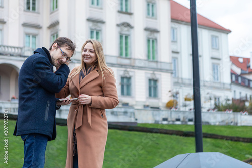 Couple smiles together while looking at a device outside a historical building in a city