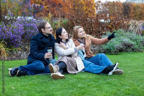 Friends sit together in a park sharing drinks and enjoying nature during autumn daylight