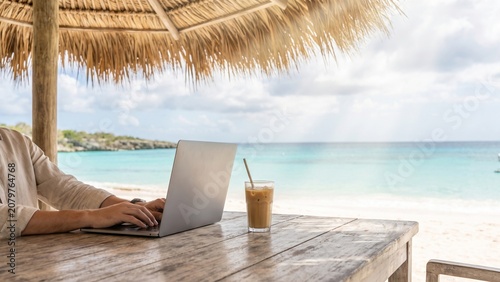 Freelancer working on laptop with iced coffee at a tropical beach resort