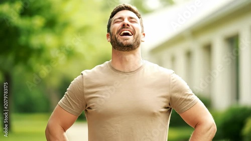 Happy man laughing outdoors with eyes closed, enjoying a joyful moment in nature.