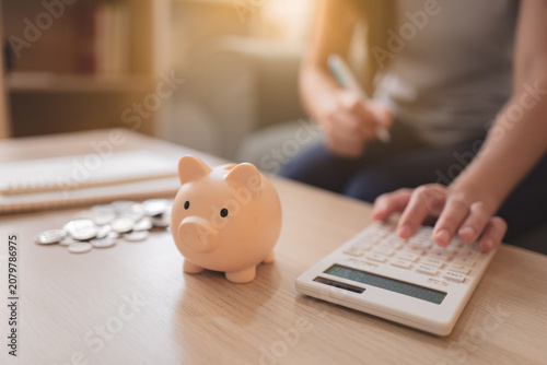 Foto Person using a calculator beside a piggy bank and coins at home, representing pe