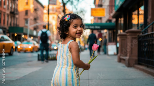 Happy little girl holding pink tulip on city street