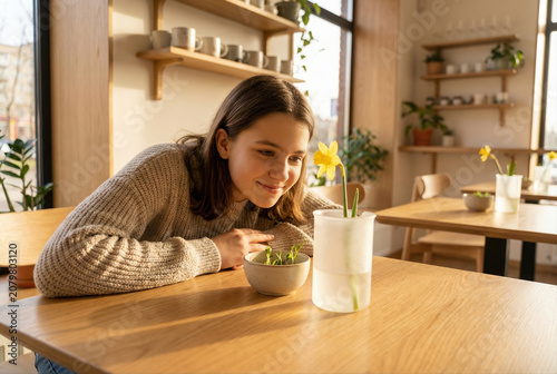 Smiling teenage girl looking at yellow flower in vase on wooden table